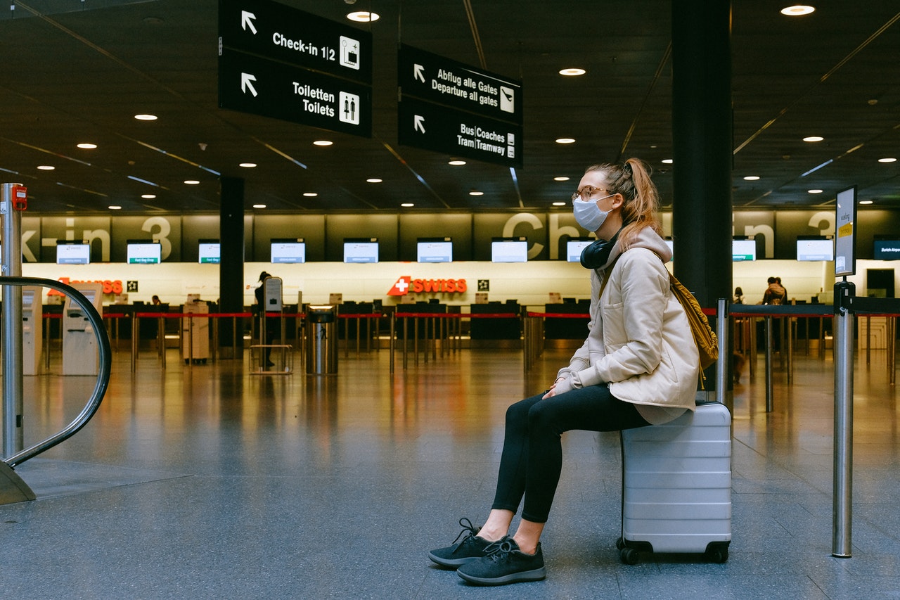 woman sitting on luggage at airport wearing a mask